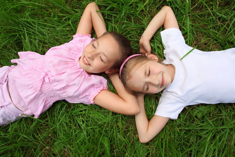 Two girls lie on grass with closed eyes