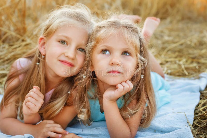 Two Girls Are Lying On A Blanket In A Wheat Field The Sisters Are Lying On A Blanket Against