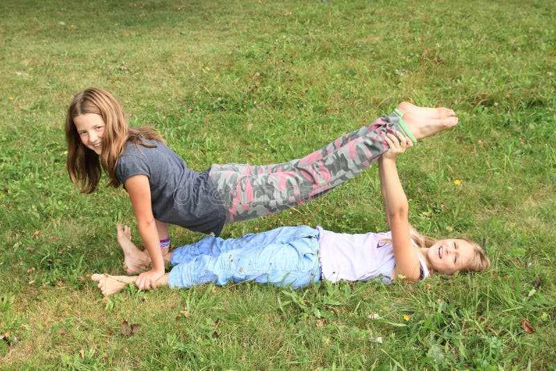 Two girls playing and exercising yoga on meadow