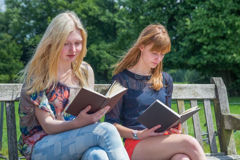 Two girls reading books on bench in nature