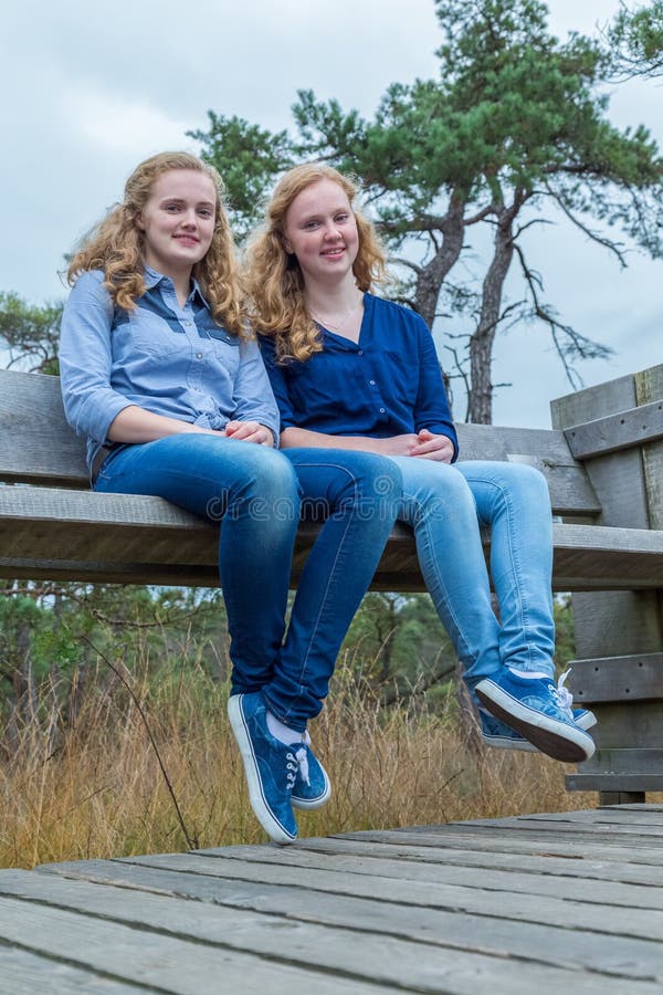 Two girls sitting on wooden bench in nature