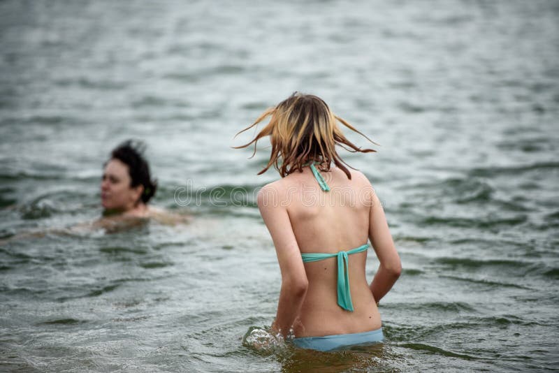 Two girls swim in the lake in the summer in cold weather.