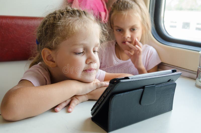 Two girls on a train with interest looking cartoon Tablet PC