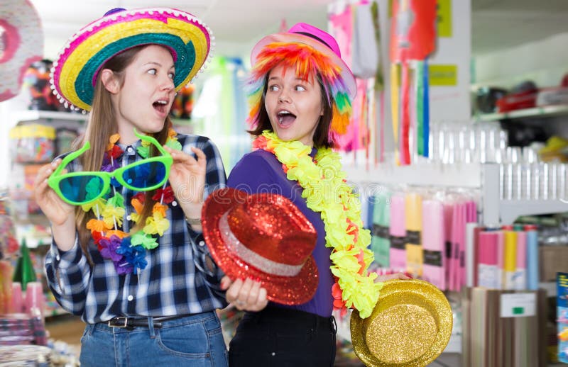 Two glad female friends choosing headdresses