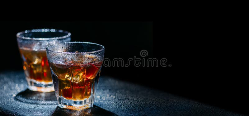 Two glass of cold alcohol cocktail drink on black background with copyspace. Whiskey with ice and cola on bar table