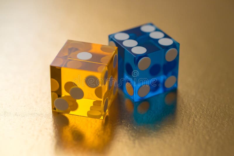 Two glass dice, yellow and blue, on a gold background in sunlight. Result one and six.