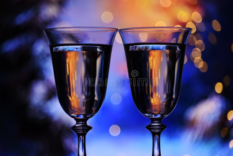 Two glasses with champagne sparkling wine on a festive blue background with lights and bokeh. Atmosphere of celebration, magic and happiness.