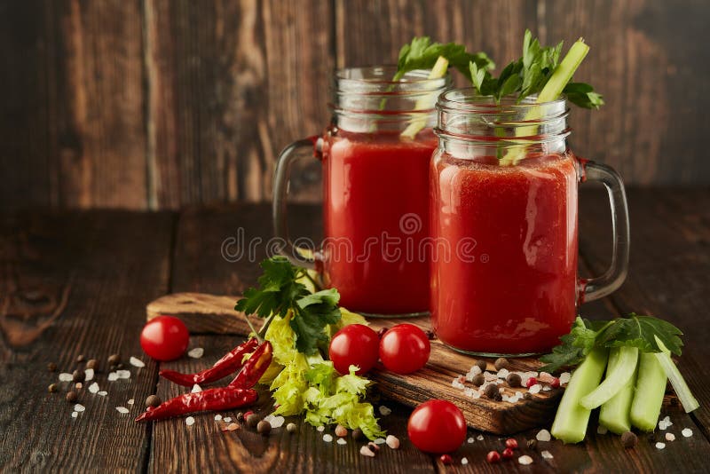 Two glasses with fresh tomato juice, celery, parsley and ripe tomatoes on dark brown wooden background