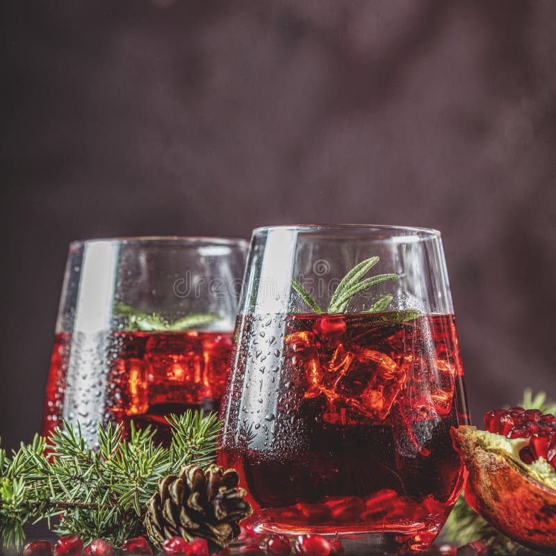 Two glasses of pomegranate drink surrounded  pine branches, claret bordeaux concrete background