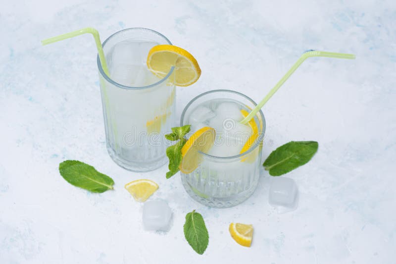 Two glasses of refreshing lemon water with ice cubes, mint leaves and straws on a light marble background. A citrus drink for a royalty free stock photo