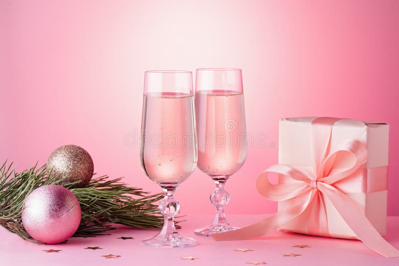 Two glasses of sparkling wine, gift box with bow, decorations. Composition in pink for Christmas, New Year. Still life with drinks and wrapped gift
