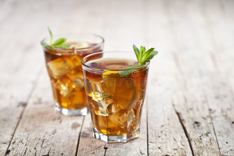 Two glasses with traditional iced tea with lemon, mint leaves and ice cubes in glass on rustic wooden table background