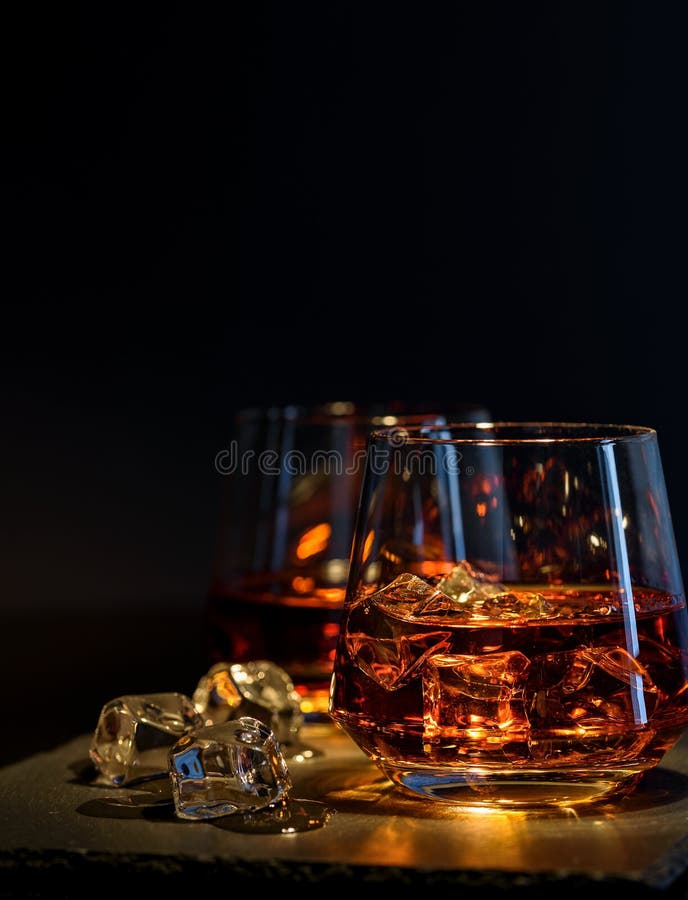 Two glasses of whiskey with ice on a black background