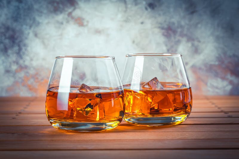 Two glasses of whiskey with ice. Still life. Brandy, bourbon on a brown wooden table. Strong alcohol drink. Rum, scotch