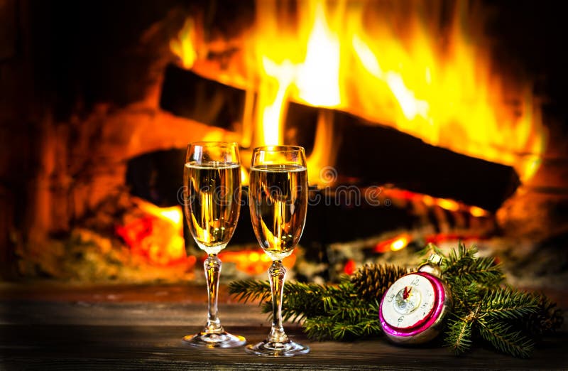 Two glasses of sparkling white wine and New Year Christmas decoration in front of warm fireplace. Romantic, cozy relaxed magical atmosphere near fire. New Year or Christmas concept. Two glasses of sparkling white wine and New Year Christmas decoration in front of warm fireplace. Romantic, cozy relaxed magical atmosphere near fire. New Year or Christmas concept
