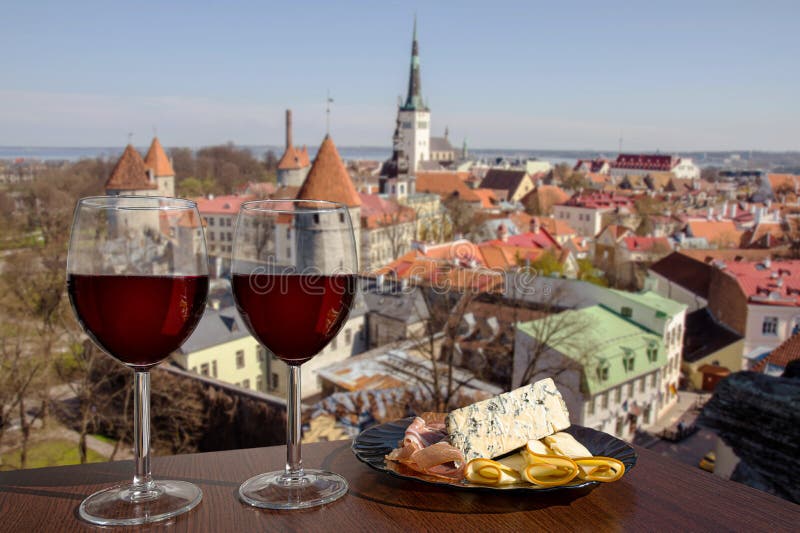 Two glasses of wine with mixed snacks against view from above of historic old town in Tallinn. Glass of red wine with different snacks - plate with ham, sliced, blue cheese. Romantic celebration. Two glasses of wine with mixed snacks against view from above of historic old town in Tallinn. Glass of red wine with different snacks - plate with ham, sliced, blue cheese. Romantic celebration