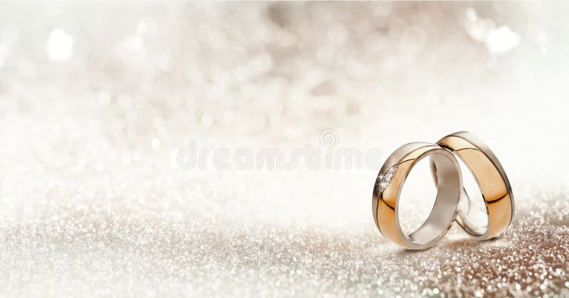 Panoramic banner of two upright gold wedding bands symbolic of love and romance on a textured glitter background with copy space for your greeting or congratulations. Panoramic banner of two upright gold wedding bands symbolic of love and romance on a textured glitter background with copy space for your greeting or congratulations