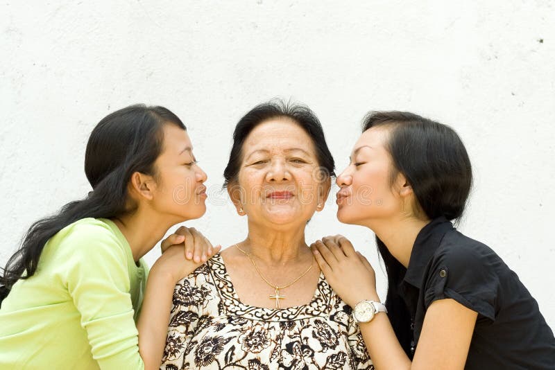 Two granddaughter kiss their old grandmother