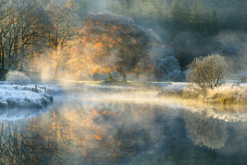 Peaceful misty morning in the English Lake District National Park with Autumn colours reflecting in still calm river.