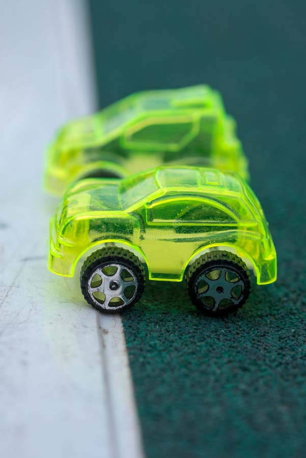 Two green toy plastic cars lined up on a white line making a point about clean fuel royalty free stock photos Two green toy plastic cars lined up on a white line making a point about clean fuel royalty free stock photos