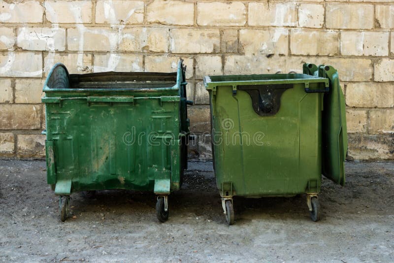 Two Green Trash Dumpsters in Front of White Brick Wall Front View with