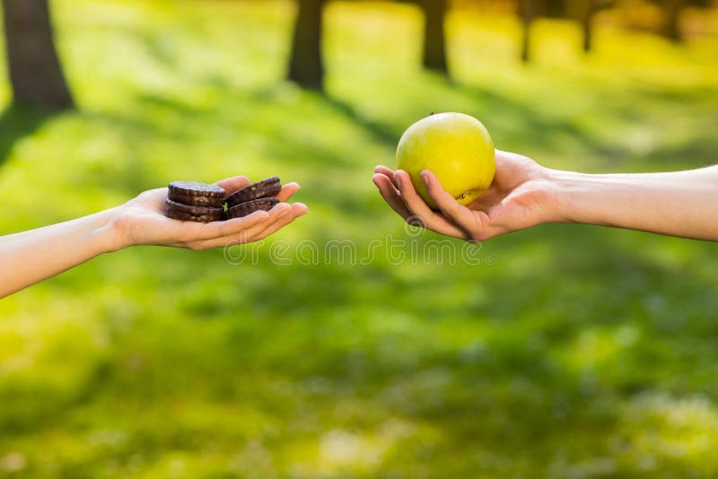 Two hands, female and male, holding and comparing cookie and apple. Background of the green park stock photo Two hands, female and male, holding and comparing cookie and apple. Background of the green park stock photo