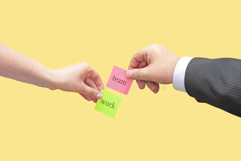 Two Hands Hold Two Sticky Notes with the Words Team and Work Stock