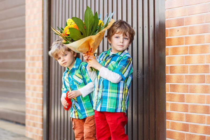 Two happy adorable little sibling boys with blooming flowers, outdoor. For mother's day or birthday congratulation.