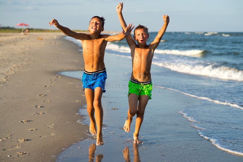 Two happy boys running on the sea beach at summer with raised ar royalty fr...