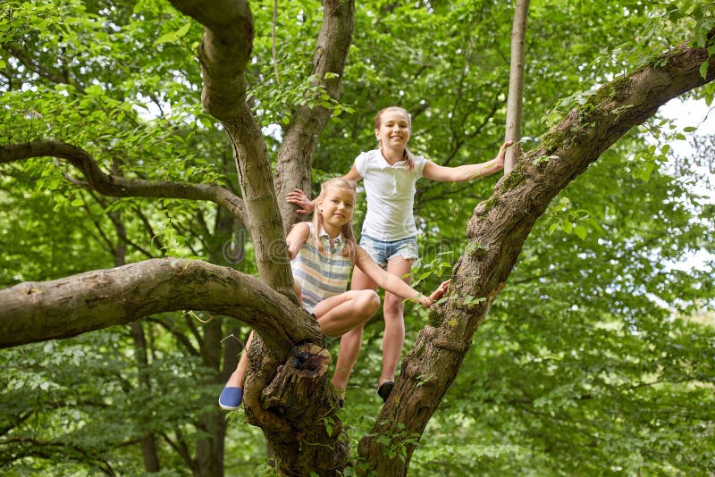 Two happy girls climbing up tree in summer park