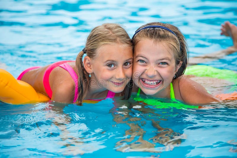 Two happy girls playing in the pool on a sunny day. Cute little girls enjoying holiday vacation