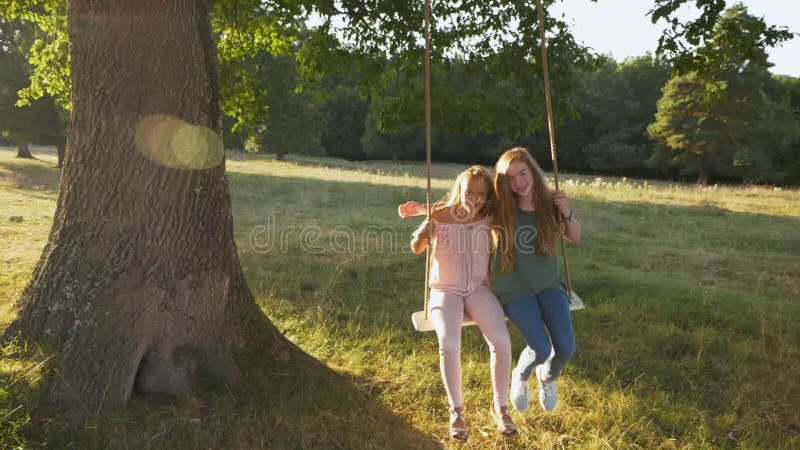 Two happy girls swinging on rope swing outdoors - slow motion