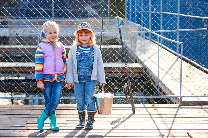 Two happy laughing children with fishing rods and a bucket on a fishing trip on a wooden pontoon on a fish farm royalty free stock photography Two happy laughing children with fishing rods and a bucket on a fishing trip on a wooden pontoon on a fish farm royalty free stock photography