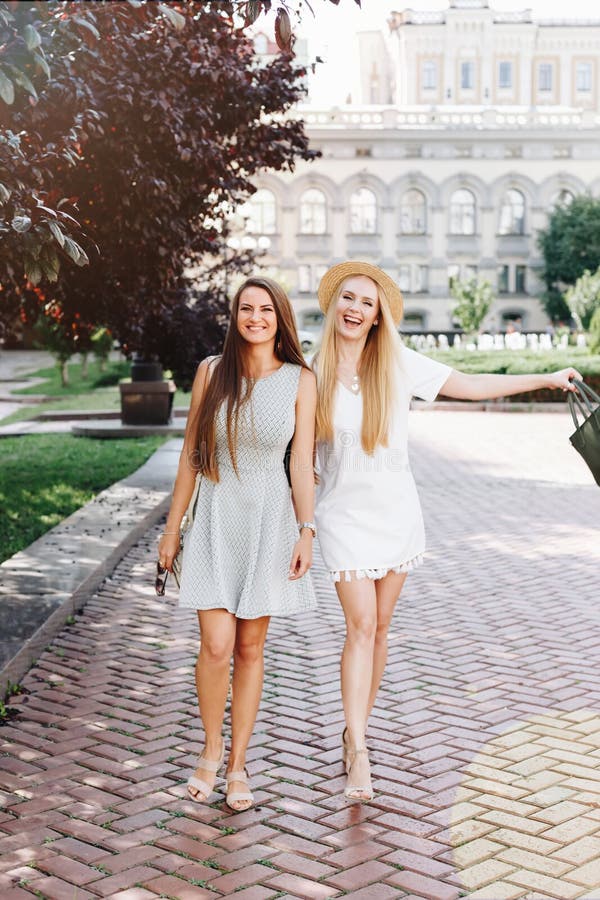Two happy smiling girls are walking in the sunny city. Beautiful blonde and brunette walking down the street, students, travelers royalty free stock photo Two happy smiling girls are walking in the sunny city. Beautiful blonde and brunette walking down the street, students, travelers royalty free stock photo