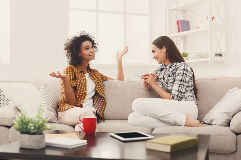 Two young female friends with coffee conversing