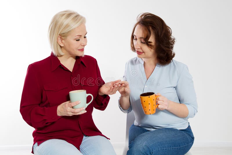 Two healthy and beautiful middle aged women drinking tea and talking isolated on white background. Woman support woman. Happy