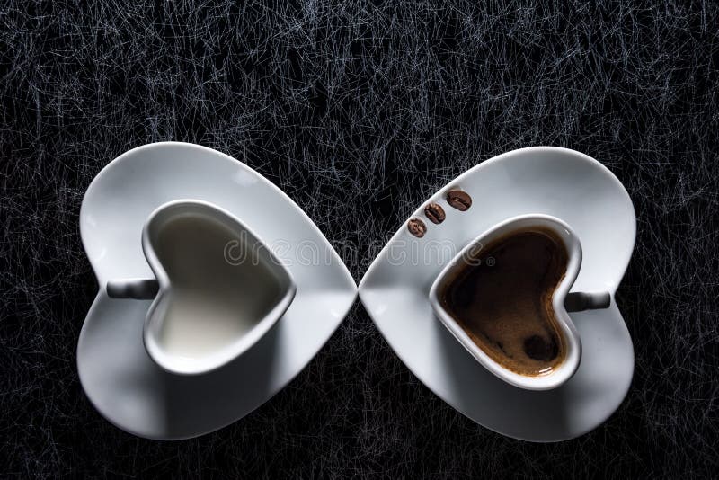 Two heart shaped cups with black coffee and milk pointing to each other, with three coffee beans royalty free stock photography Two heart shaped cups with black coffee and milk pointing to each other, with three coffee beans royalty free stock photography