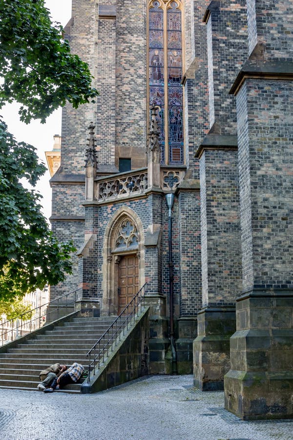 Two unrecognizable homeless men sleep in the shadows on the bottom steps of staircase of Gothic cathedral in old center of Prague, Czech Republic, hot summer day. Two unrecognizable homeless men sleep in the shadows on the bottom steps of staircase of Gothic cathedral in old center of Prague, Czech Republic, hot summer day