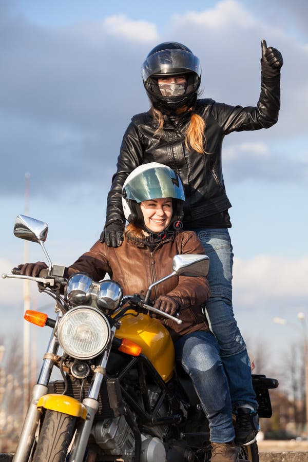 Two joyful European women driving motorcycle, girl standing behind with thumb up royalty free stock image Two joyful European women driving motorcycle, girl standing behind with thumb up royalty free stock image