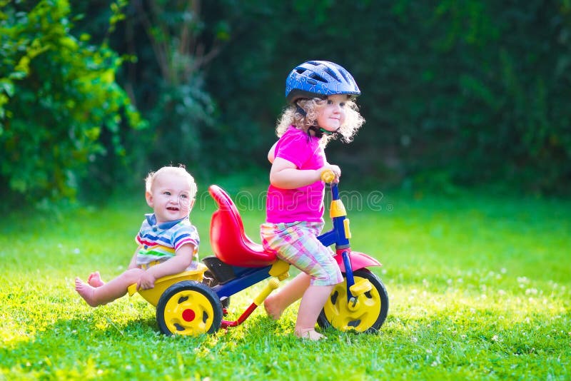 Children riding a bike. Kids enjoying a bicycle ride. Little preschooler girl and baby boy, brother and sister, having fun outdoors. Active toddlers play in the garden. Children riding a bike. Kids enjoying a bicycle ride. Little preschooler girl and baby boy, brother and sister, having fun outdoors. Active toddlers play in the garden.