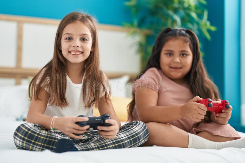 Two Kids Playing Video Game Sitting on Bed at Bedroom Stock Photo