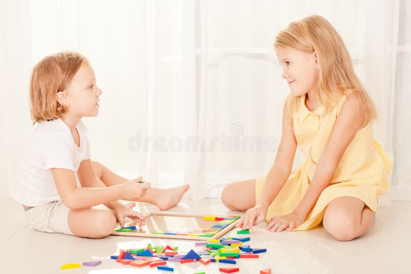 Two kids playing with wooden mosaic in their room on the floor