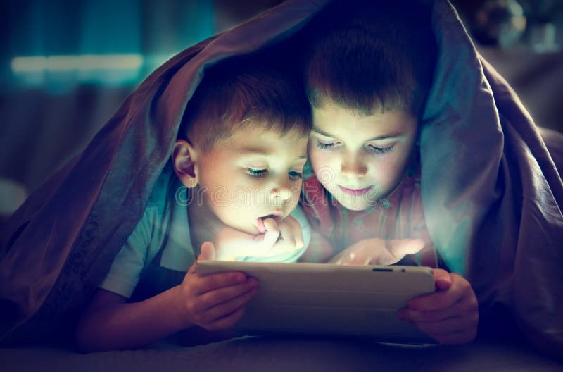 Two kids using tablet pc at night royalty free stock photography