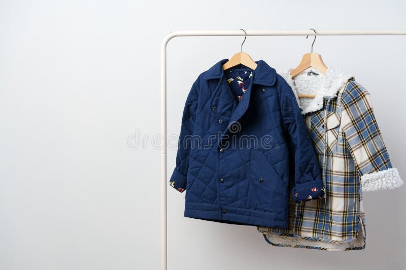 Two Kids Winter Coats Hanging on Hangers Against White Wall Stock Image
