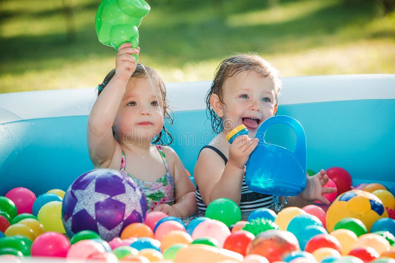 The two little baby girls playing with toys in inflatable pool in the summer sunny day stock photo The two little baby girls playing with toys in inflatable pool in the summer sunny day stock photo