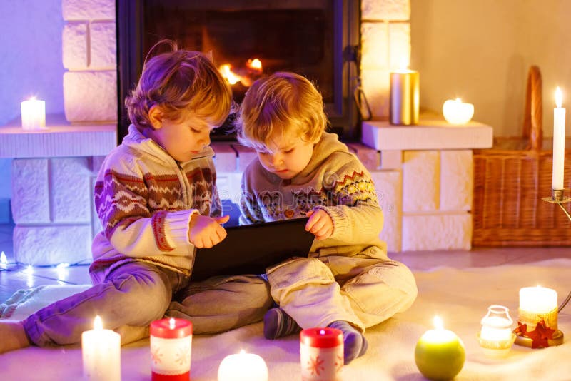 Two little children sitting by a fireplace at home on Christmas time. Happy cute adorable toddler boys, blond twins stock images Two little children sitting by a fireplace at home on Christmas time. Happy cute adorable toddler boys, blond twins stock images