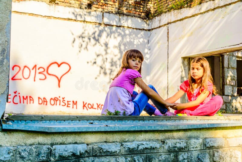 Two little girls are sitting on the old window opening and are holding hands. Two little girls are sitting on the old window opening and are holding hands