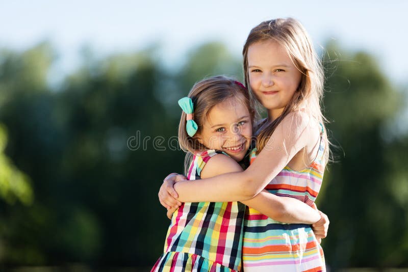 Two little girls hugging each other in the park.