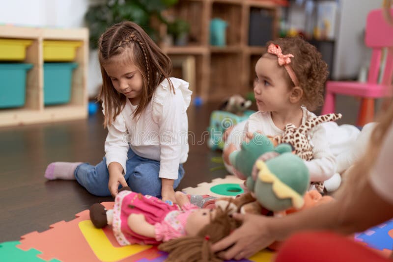 Two Little Girls Playing with Dolls Sitting on Floor at Kindergarten