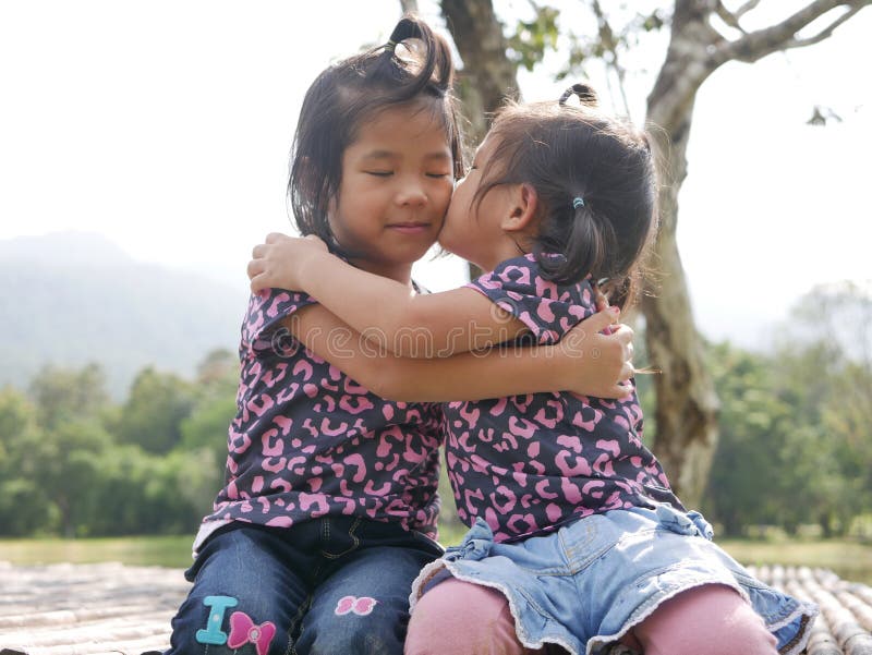 Two little girls, sisters, hugging and kissing on a bench in the evening sunlight - sisters` bond and love